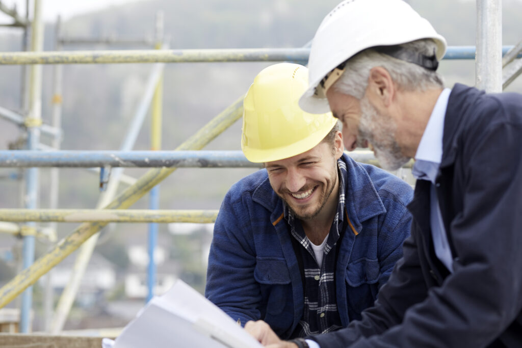 Happy architect and worker discussing building plan on scaffolding on a construction site